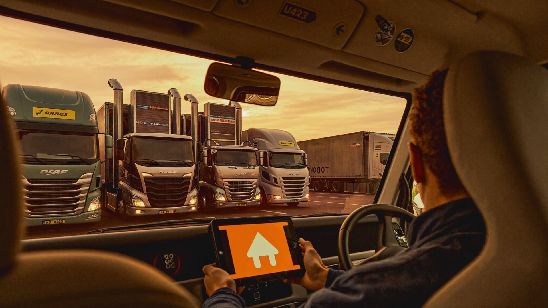 Truck driver using dispatch tablet in cab with loading dock visible through windshield
