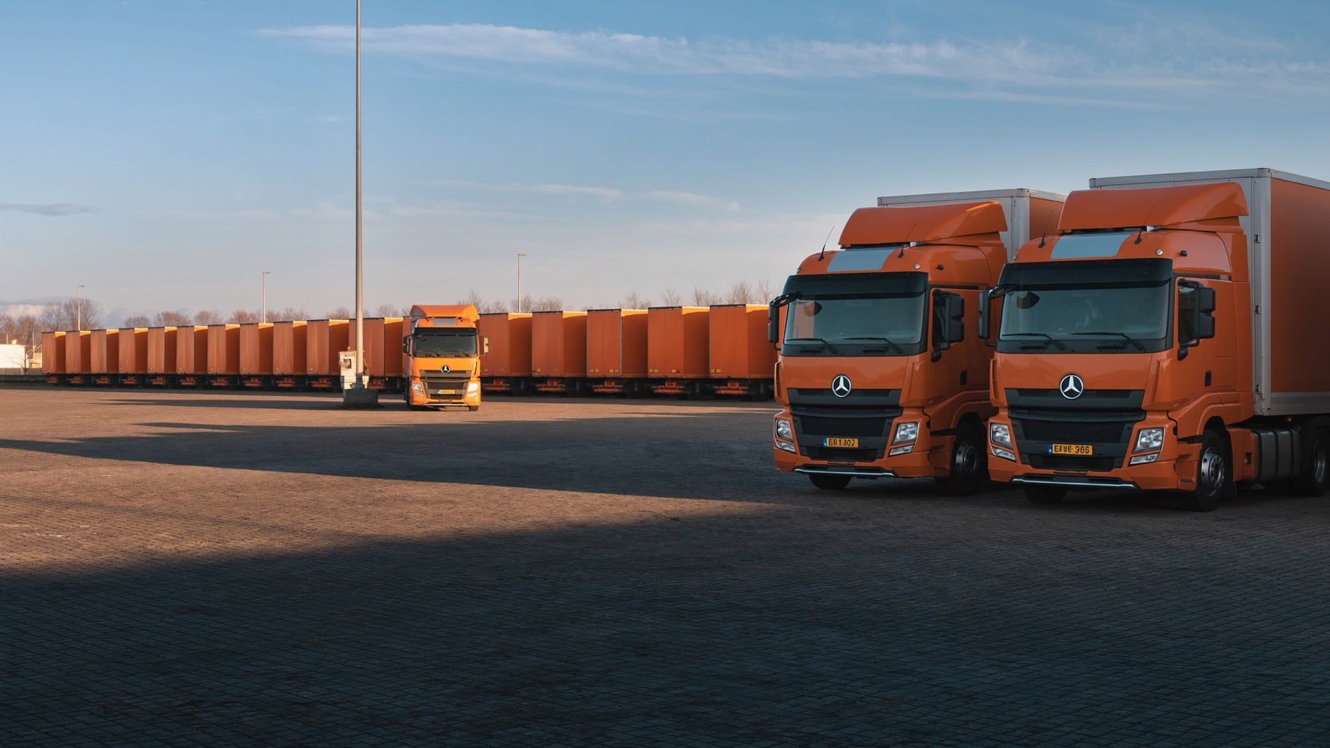 Fleet yard at dawn with rows of semi-trucks and a driver walking to start the day